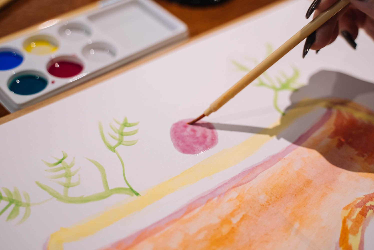 CLose up of a person painting a simple scene with watercolour paints